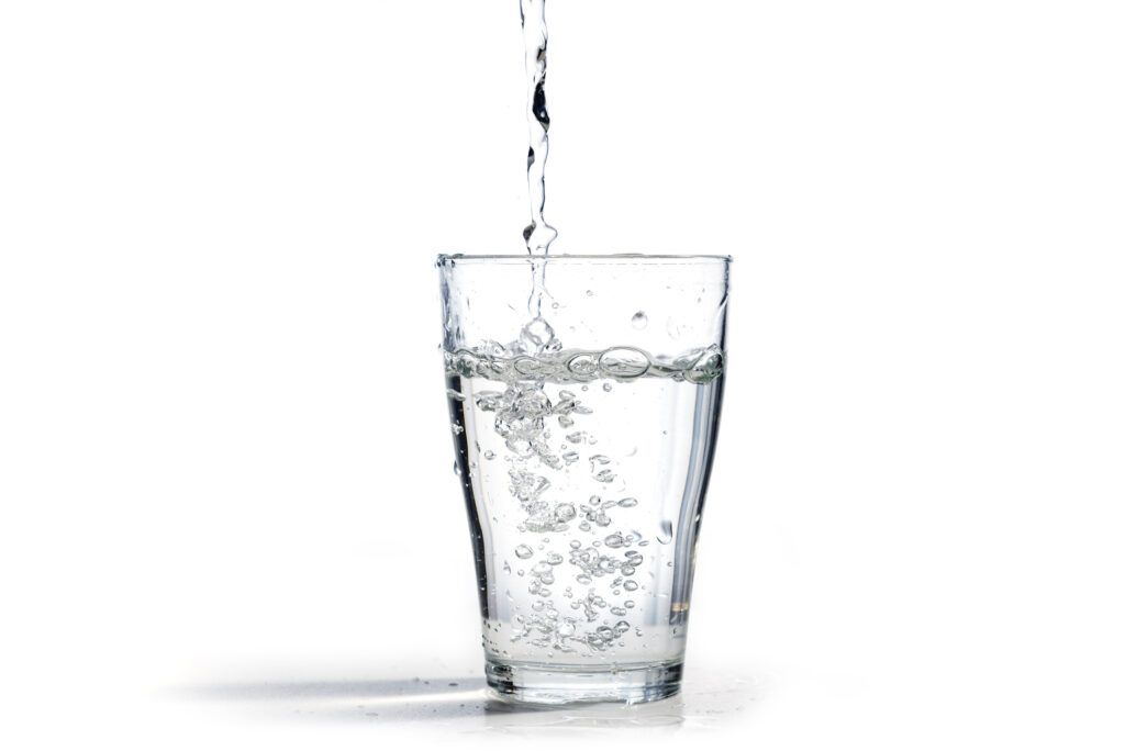 Water Is Poured Into A Drinking Glass, Isolated On A White Background With Copy Space