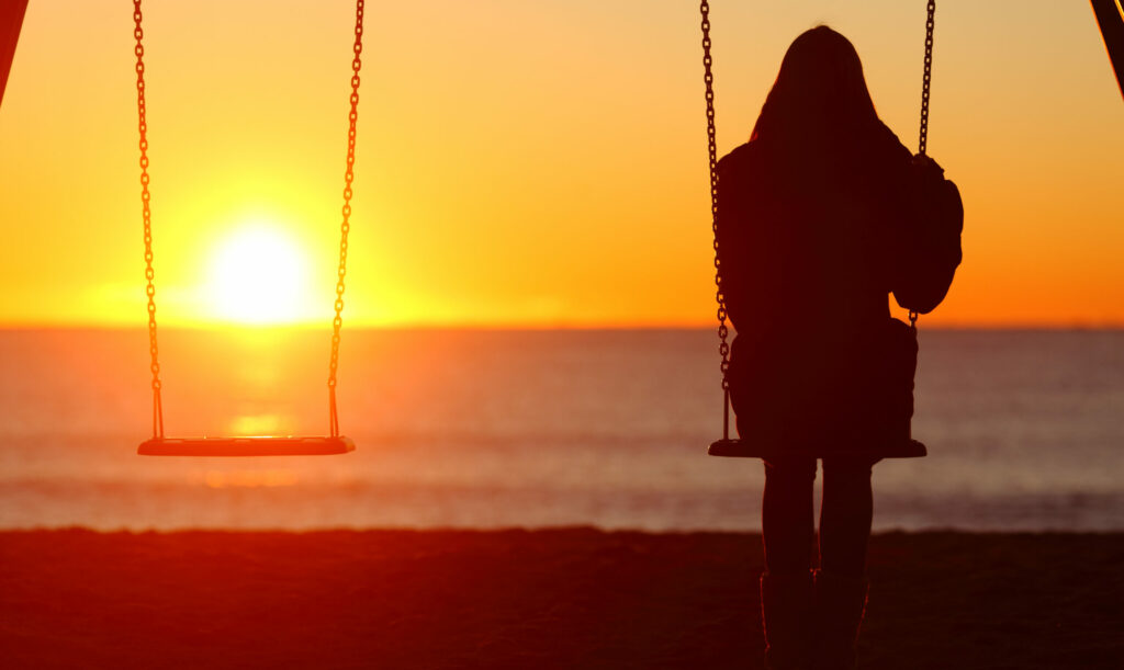 Single Woman Sitting On A Swing Contemplating Sunset