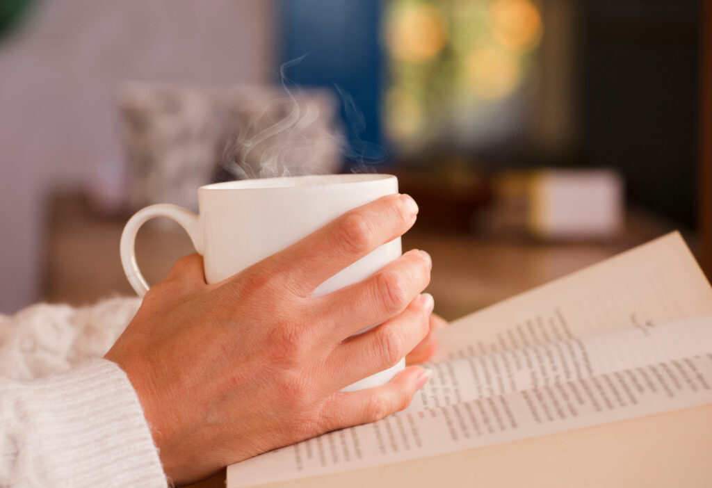 White Cup With Hot Drink And Smoke, Hands Warming Up From The Heat, At Home. Focus On The Cup.