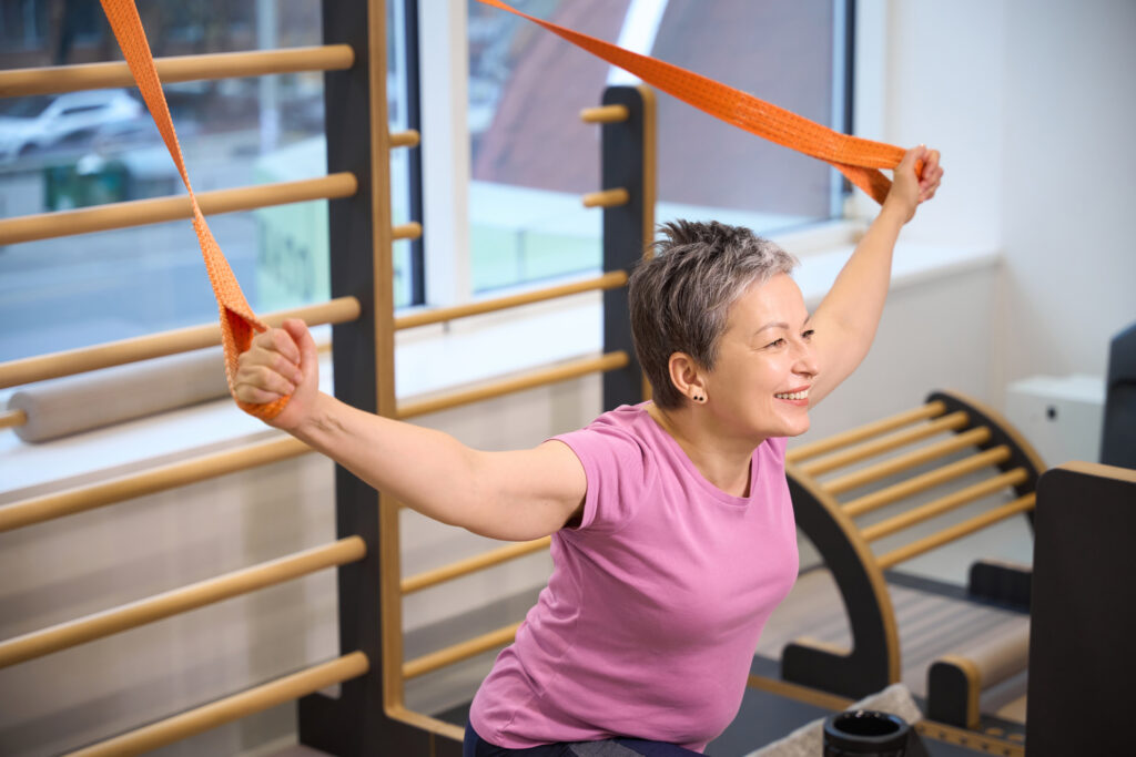 Smiling Mature Caucasian Woman Stretching With Rope In Rehabilitation Gym