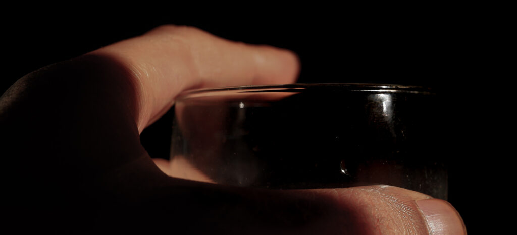 Close Up Of Hands Holding A Glass Of Drink In A Low Light Room